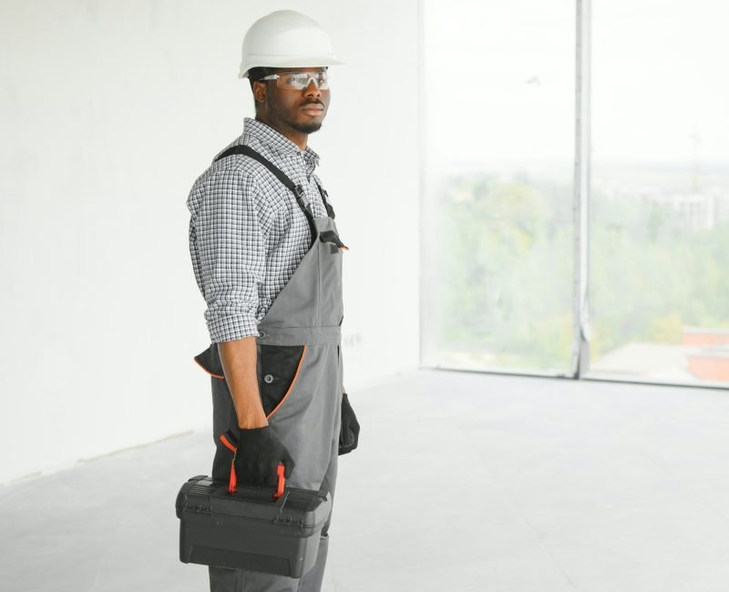 Portrait of handsome young african american male builder in hard hat, working at construction site